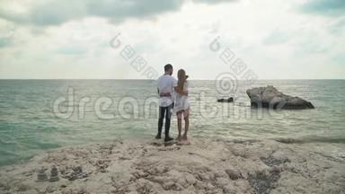站在海边的年轻夫妇要欣赏美丽的海景。 男人和女人互相拥抱。 年轻人的休闲