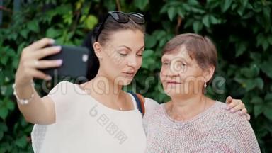 美丽的老奶奶和她的孙女在树叶背景下户外自拍，看着相机，微笑着。