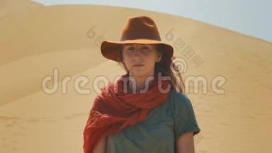 肖像：沙漠中的女孩旅行者在沙滩上。 戴着帽子和红领巾.. 探索古老的地形，寻找