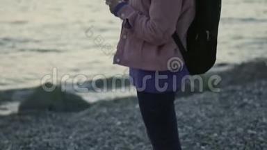 日落时分，一位年轻女子戴着智能手机和蓝牙耳机站在海滩上的肖像