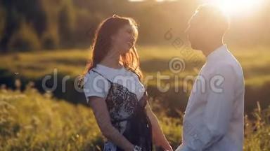 夏天日落时分，年轻的男女在草地上漫步。 浪漫。 夏日的爱情相聚欢乐浪漫的回忆