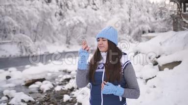 女孩在近山河的冬天森林里用手机视频交谈。