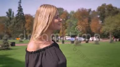 一位金发的白种人满意的女士正在阳光明媚的天气和光线下直看公园
