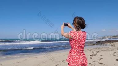 年轻迷人的女人拿着相机电话，为矗立在塞浦路斯海滩上的风暴海浪拍照。 慢动作