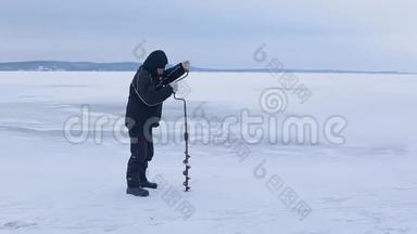 穿着深色衣服的渔夫用冰钻在冰冻的河流上<strong>挖洞</strong>