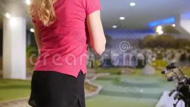 打迷你高尔夫。 一位年轻女子在室内打迷你高尔夫。 击球，把球棒放在肩上