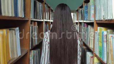 一位美丽的年轻女子走在图书馆的书架之间。 概念：教育