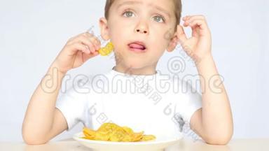 一个高兴又高兴的孩子，吃着<strong>薯片</strong>，坐在桌子旁的白色背景上，特写..