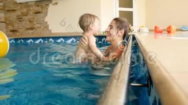 4k慢速动作镜头快乐微笑的母亲抱着孩子在游泳池里吐气