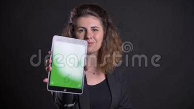 集中超重的白种人妇女在平板电脑上工作的特写照片显示了黑色背景下的绿色屏幕。