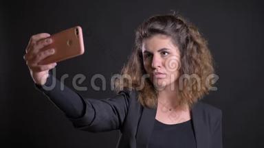 在<strong>黑色背景</strong>下使用智能手机制作自拍<strong>照片</strong>的超重高加索妇女的特写肖像。
