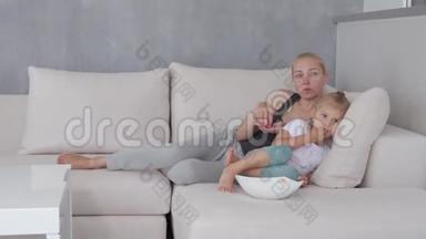 一个女人和一个小女孩坐在柔软的沙发上，吃着爆米花，看着电视<strong>屏</strong>幕。
