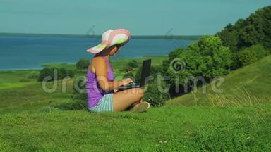 一个<strong>戴草帽</strong>的女人坐在俯瞰湖的山上，关上笔记本电脑的盖子。