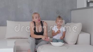 一个女人和一个小女孩坐在柔软的沙发上，吃着爆米花，看着<strong>电视屏幕</strong>。