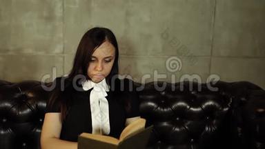 女人在沙发上看书。 20多岁的肖像妇女在明亮的沙发上休息和坐着，还在看书