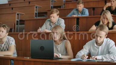 一大群多民族学生在笔记本电脑上工作，同时在现代课堂上听讲座。 明亮明亮