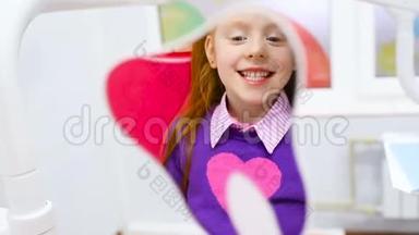 一个红头发的小<strong>可爱女孩</strong>在坐在牙科椅上的镜子里欣赏她健康的牙齿。