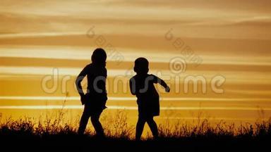 两个孩子在日落时跳舞，享受大自然。 幼儿`的剪影.. 快乐的孩子玩得开心，享受大自然。