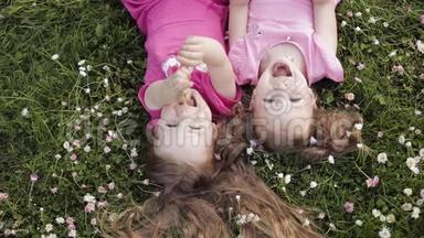 两个可爱的小女孩倒躺在草地上和鲜花上，做着空中亲吻和挥手
