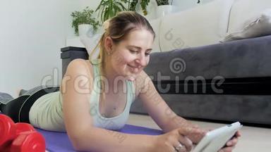 年轻女子在地板上锻炼的4K视频。 她正在看如何在平板电脑上做运动和伸展运动
