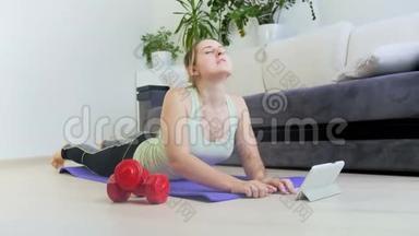 年轻女子在地板上锻炼的4K视频。 她正在看<strong>如何</strong>在平板电脑上做运动和伸展运动