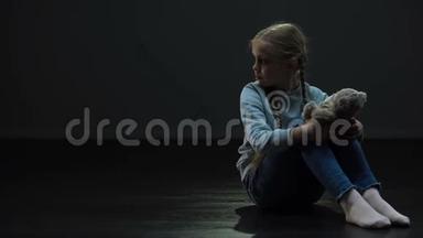 小女孩带着泰迪熊独自坐在黑暗的房间里，<strong>四处</strong>张望，孤儿