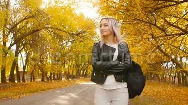 年轻漂亮的女孩走在秋天的跑道上，一个穿着皮夹克和运动服的年轻时髦女人走在沥青路上