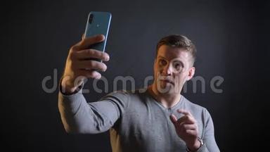 中年白种人用智能手机在黑色背景下制作自拍照片的特写肖像。