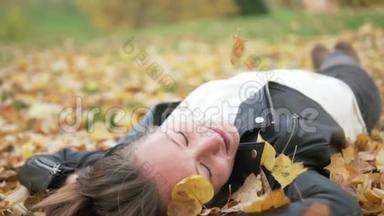 一个美丽的年轻女子躺在树<strong>下</strong>的黄色叶子上。