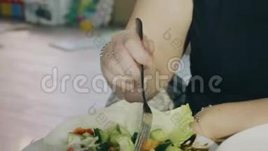 餐馆里的女孩吃着一盘白色盘子里的蔬菜沙拉。 女孩手中的银叉. 特写镜头