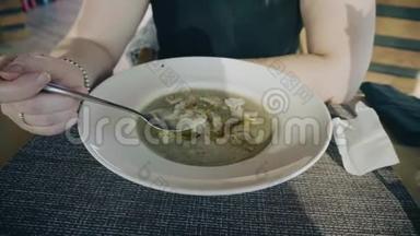 女孩坐在餐厅的桌子上，吃着汤泥白色的盘子。 不错的待遇。 镜头拍摄一张桌子，一个盘子和一个杯子