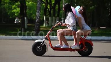 在公园里，两个头发松松的年轻和黑发朋友穿着短牛仔短裤，骑着电动摩托车骑着一辆电动摩托车