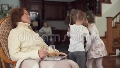 坐在摇椅上的成熟女人和她可爱的小孙女来到她身边亲吻并轻轻拥抱