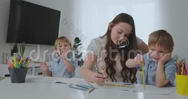 一位带着两个孩子在手机上说话的年轻母亲用铅笔画画，并帮助孩子们用彩色画画