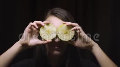 一个深黑的背景下，一个深黑的女孩眼睛上戴着一个苹果水果。 健康饮食，饮食，眼部健康理念..
