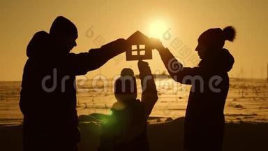 一家人在日落时分抱着纸房，梦见自己的家.. 日落时分手中的纸房剪影