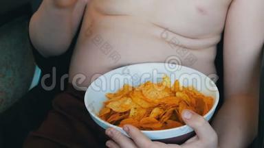 肥胖的少年身体上有脂肪褶皱，正在吃薯片.. 不健康食品，快餐.. 儿童`营养问题