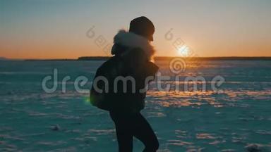 一个年轻快乐的女孩旅行者的剪影，带着背包在日落时去，冬季旅行，生活方式，自由的概念。