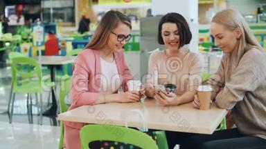 漂亮的学生正在使用智能手机坐在咖啡馆里，看着屏幕，然后做击掌和击掌