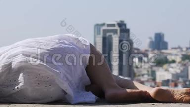 穿着白色连衣裙的女人躺在屋顶上观看城市景观，放松大胆的人
