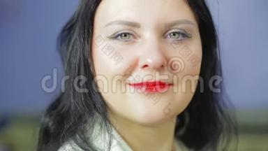 微笑的女人的脸，嘴唇上涂着鲜红的口红，手里拿着口红。 特写镜头。 聚焦翻译