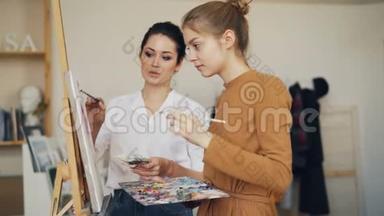 迷人的艺术<strong>学生</strong>女孩在有经验的女老师的<strong>指导</strong>下在工作室画画。 师父在说话