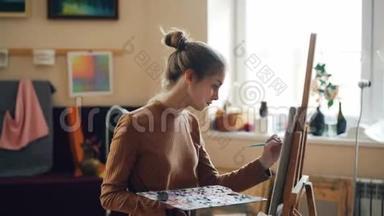 漂亮的金发碧眼的人正在画画布上画漂亮的花，独自站在画架前，用画笔和画笔