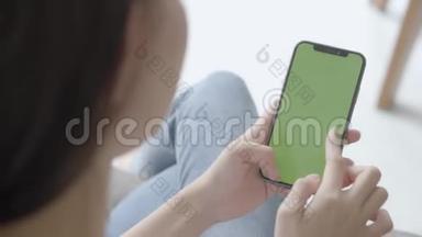 亚洲女人手牵着手，看着用绿色屏幕的智能手机在沙发上自己定制内容