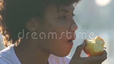 美丽的非洲裔美国妇女在城市大街吃苹果，健康的小吃