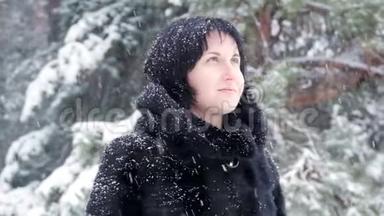 一个穿着毛皮大衣的黑发女人站在一个冬天的公园里，缓慢地看着飘落的雪。