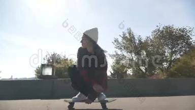 穿着白色帽子和格子衬衫的滑板女孩在户外玩滑板。 嬉皮士女孩在公园玩滑板