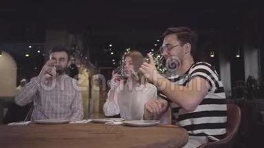 两个男人和女人坐在现代土耳其餐馆的桌子旁，用红酒叮叮当当地眨着眼睛。 朋友们