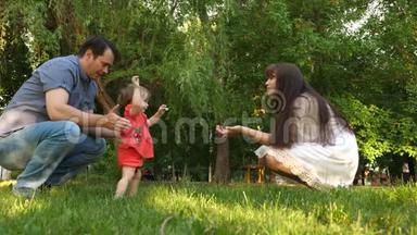 爸爸和妈妈学习在绿草地上公园里散步小女儿.. 妈妈亲吻女儿的脸颊，和爸爸一起笑。