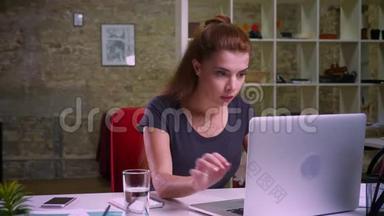 集中姜黄白种人的女人在笔记本电脑上打字，一边平静地坐在她的现代生活中，一边晃晃悠悠